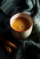 Cup of warm coffee with cinnamon and a vintage blanket on dark background