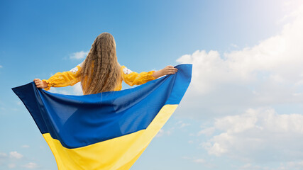 Girl carries fluttering blue and yellow flag of Ukraine in field.