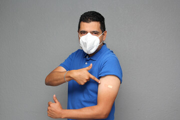 Happy Latino adult man shows his arm that just received the Covid-19 vaccine and has an adhesive band in the new normal of the pandemic
 - obrazy, fototapety, plakaty