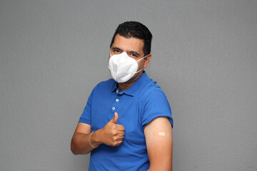 Happy Latino adult man shows his arm that just received the Covid-19 vaccine and has an adhesive...
