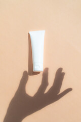 Shadow hand gesture tube cosmetic. Natural skincare white beauty product on beige background. Facial skin treatment mockup.