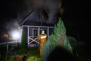 Fototapeta na wymiar Firemen extinguish fire in rural house at night