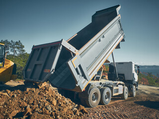 Unloading tipper. Earthmoving works at construction site. Dump truck unloads soil from truck back