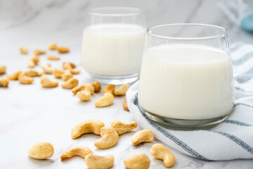 Glasses of vegan milk with heap of cashew nuts on kitchen towel on marble background. Lactose free non-dairy milk drink. Alternative types of milks. Vegan food concept.