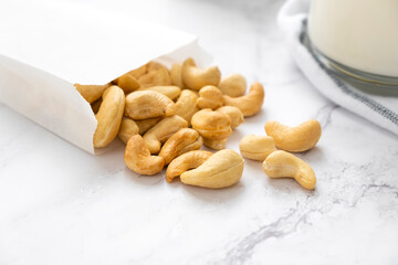 Glass of vegan milk with cashew nuts in white packet on marble background. Lactose free non-dairy milk drink. Alternative types of milks. Vegan food concept.