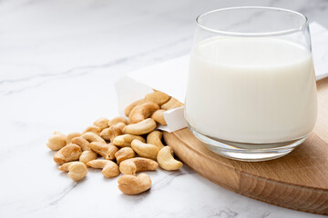 Plant based milk with heap of cashew nuts on wooden board on marble background. Lactose free non-dairy milk drink. Alternative types of milks. Vegan food concept.