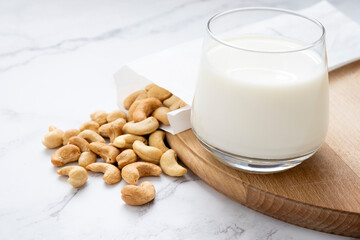 Glass of vegan cashew milk with heap of nuts on wooden board on marble background. Lactose free non-dairy milk drink. Alternative types of milks. Vegan food concept.