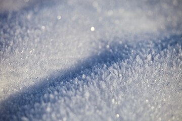 White ice crystals in bright sunlight. Macro photography of ice crystal texture. Snow crystals close-up on a bright frosty winter day. White sparkling snow surface close up. Abstract snowy pattern.