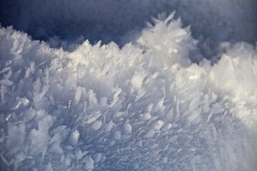 White ice crystals in bright sunlight. Macro photography of ice crystal texture. Snow crystals close-up on a bright frosty winter day. White sparkling snow surface close up. Abstract snowy pattern.