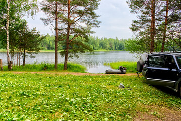 Rest and fishing in nature. A picturesque place on the lake. A car, an inflatable boat on the shore...