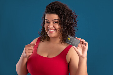 young woman with curly hair smiling and holding a credit card and pointing it with her finger