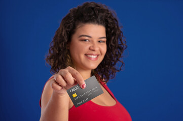 latin american young woman holding a credit card and showing it to the camera on a blue background