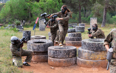 Dynamic paintball battle, players jumping and aiming with guns outdoors