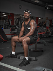 Fototapeta na wymiar African american sports man sitting on sport bench. Handsome smiling powerful athletic guy in gym