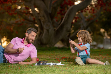 Father and son playing chess outdoor in park.