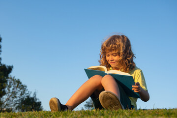 Smart kid boy reading book in park outdoor.