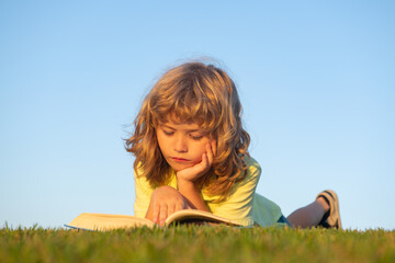 Outdoor school, motivation learning kids. Child boy reading book, laying on grass in field on sky background. Portrait of clever kids.