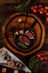 Fototapeta na wymiar Grilled slices cap rump steak with rosemary branch, golden forks and spices on wooden cutting board (Brazilian picanha) - Top view.