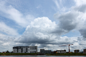 Fototapeta premium Exterior facade of newly build luxury apartment building Kade Noord next to construction site of Kade Zuid with river IJssel in the foreground and large cumulus raincloud above