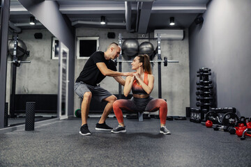 Fototapeta na wymiar The concept of sports personal training. A fitness man and a slender woman do sports exercises together. The lady is in the cone position while the trainer corrects her body position