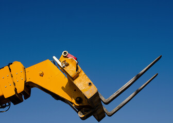Forks of the Telescopic Forklift Telehandler raised on the blue sky background