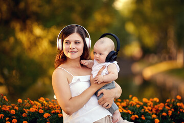 Mother and infant in wireless headphones sit in park.