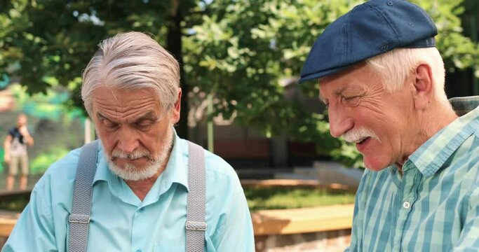 Caucasian old best friends playing cards game at the fresh air and making their turns on the wooden table. Outdoor.