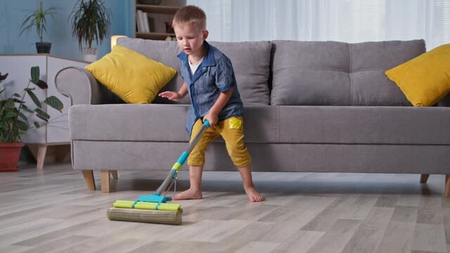 house cleaning, little hardworking male child helps parents and mops floor with colored mop in room