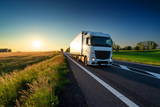 White truck driving on the asphalt road in rural landscape at sunset