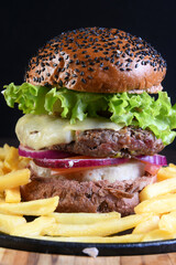 delicious gourmet burger sandwich with cheese, salad, pickles and sesame bread isolated on black background.