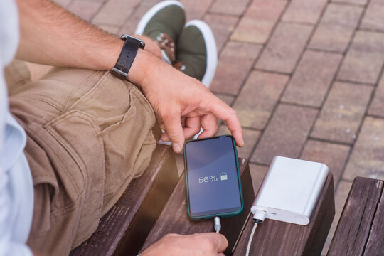 Man charges a smartphone with a power bank in hand. Portable charger for charging gadgets.