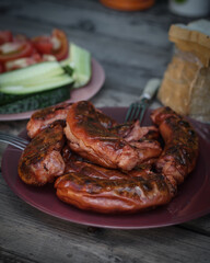 Hot sausages from the grill on a plate. Serving with bread and vegetables on a wooden table.
