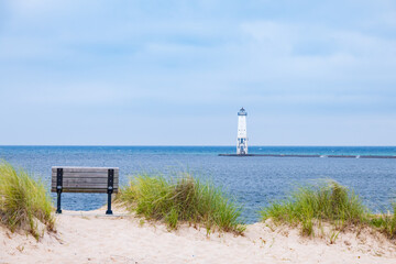 Fototapeta na wymiar Wooden bench overlooking Lake Michigan and Frankfort North breakwater lighthouse in background