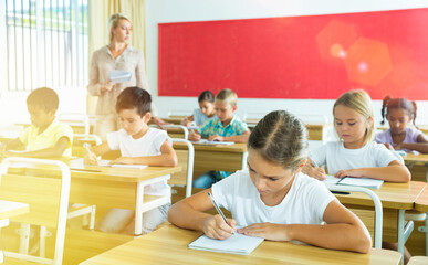 Fototapeta na wymiar Attractive smart preteen girl studying in classroom, listening to teacher and writing in notebook