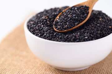 Black sesame seeds in a white bowl with wooden spoon, Food ingredients