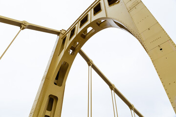 Close structural details of a self anchored suspension bridge painted yellow, overcast sky, horizontal aspect