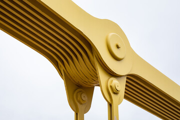 Close up detail view of a suspension bridge joint, metal plates painted yellow isolated against a white sky, horizontal aspect