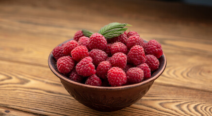 Bowl with fresh ripe delicious raspberries and a green leaf on a wooden background