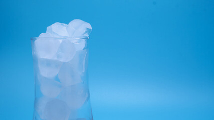 Close-up shot, showing the ice in clear glass of water melting on copy space blue background as the temperature rises. Media about global warming from world climate change and the greenhouse effect.