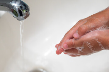 The hands of a small toddler being washed in a white bathroom sink.