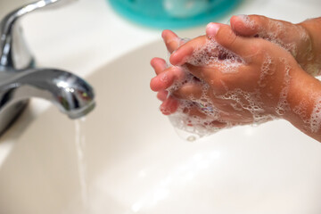 A small child's hands being washed with soapy foam in a white bathroom sink