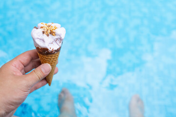 man sitting on the edge of an outdoor swimming pool and eating an ice cream cone
