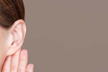 Girl put her hand to her ear and listens attentively on brown background.