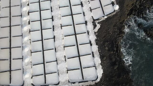 Overhead shot of white salt evaporation ponds; rocky coastline adjacent