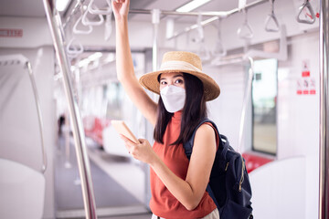 Fototapeta na wymiar Asian woman wearing face mask and using smartphone on subway train,Safety on public transport,New normal during covid-19 pandemic.