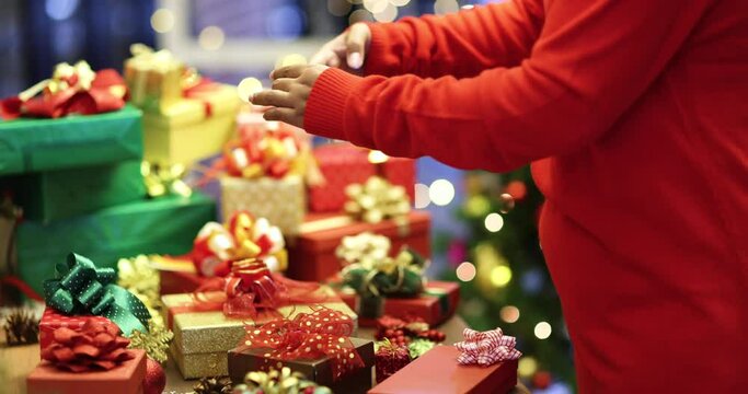 Woman in red sweaters holding and using smartphone taking photos of various sizes Xmas gift boxes with bokeh lights in blur background. Idea for happy and joyful life in Christmas festival.