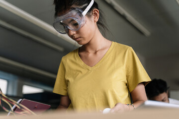 Young Asian Student Girl with protective glasses learning robotics and software engineering-...