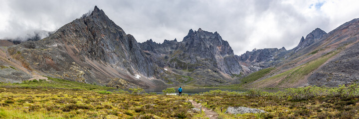 Fototapeta na wymiar Backcountry camping area of Tombstone Territorial Park off Dempster Highway during summertime on a cloudy morning from the Grizzly Lake hiking trail with hiker in blue jacket. 