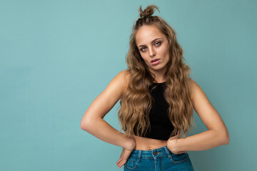 Shot of young upset sad pretty blonde woman wearing black top isolated on blue background with empty space and having questions