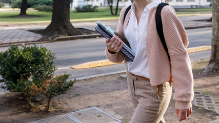 Back to school concept. Body part of young female student walking down the street, carrying with folders and backpack.